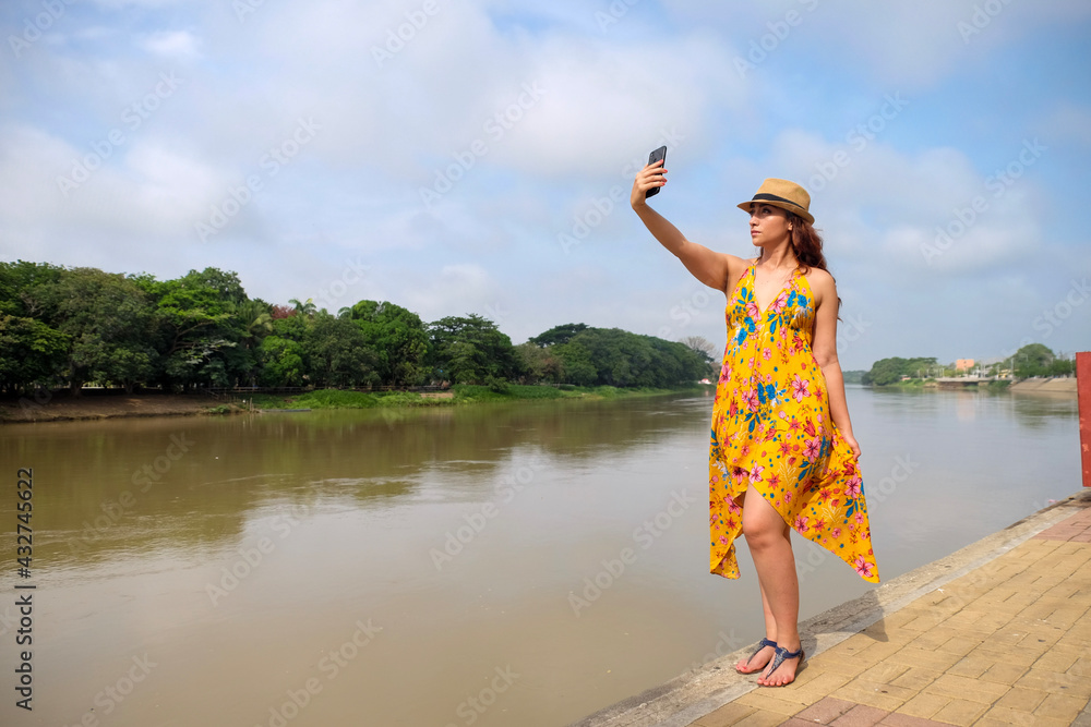 woman in yellow dress taking a selfie by the river