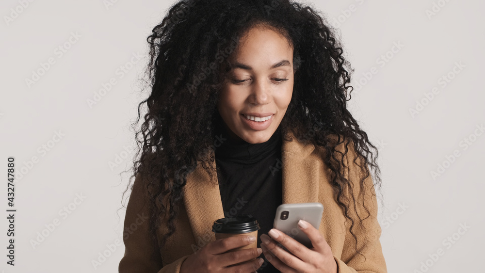 Beautiful African American woman using smartphone and drinking take away coffee over white background. Modern technology Beautiful African American woman using smartphone and drinking take away coffee over white background. Modern technology