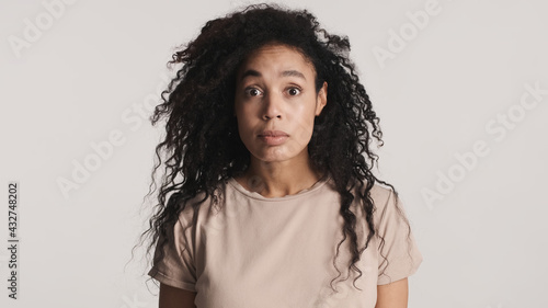 Afro woman with dark curly hair looking shocked posing on camera