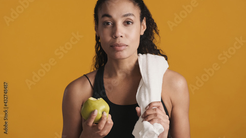 Young confident Afro woman dressed in sport bra eating apple aft