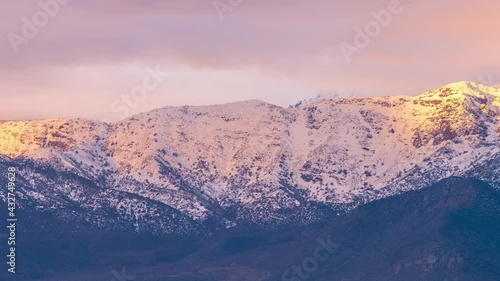 An amazing view of the snow covered Andes mountains fields with the sunlight coming from the sunset on a cloudy day. A time lapse view to see the clouds motion