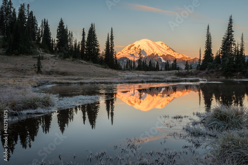 The volcanic peak in Mount Rainier National Park reflects in Upper Tipsoo Lake at dawn. This mountain is known to the American Indian peoples as Mount Tahoma. Ice is along the edge of the water