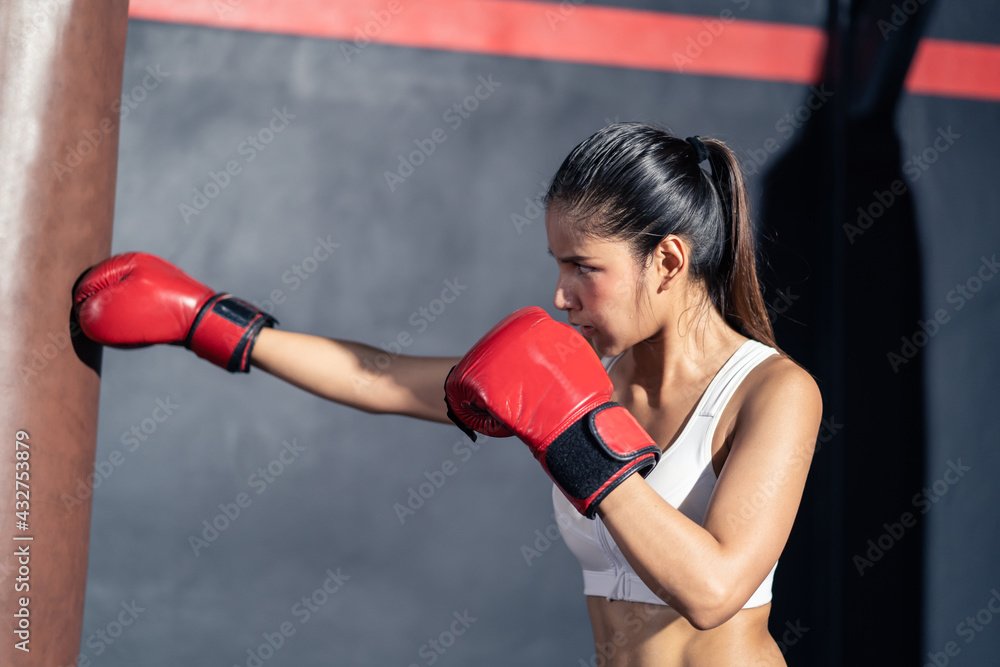 Asian beautiful sportswoman punching heavy bag for exercise in gym.