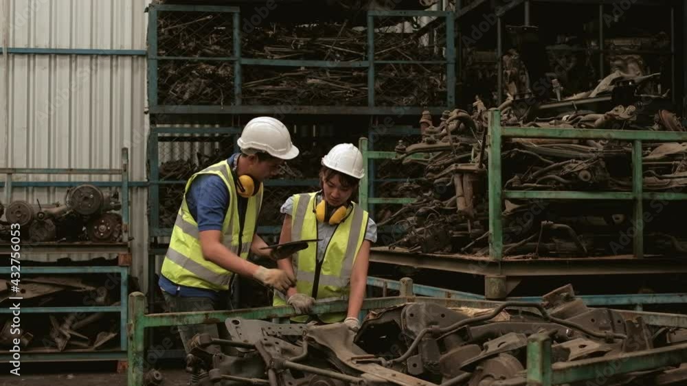 Asian male and female workers in uniforms and helmets, Employee stock check of car spare parts warehouse factory. Using a tablet to check old engines and machine orders for automotive industry. Asian male and female workers in uniforms and helmets, Employee stock check of car spare parts warehouse factory. Using a tablet to check old engines and machine orders for automotive industry.