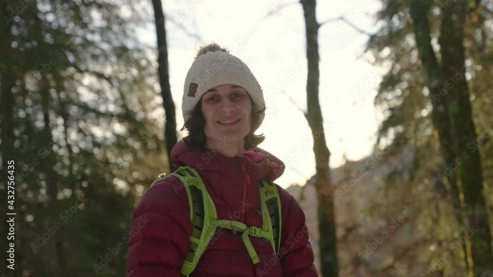 Woman smiling into the camera with sun light behind in cold forest Woman smiling into the camera with sun light behind in cold forest
