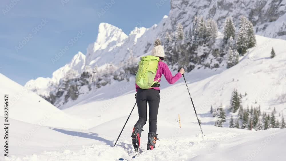 Young athletic woman walking in snow with pair of skis and poles Young athletic woman walking in snow with pair of skis and poles