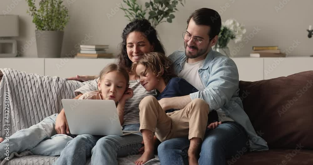 Smiling affectionate young family couple relaxing on weekend with small son and daughter, using computer software applications together, watching funny cartoons, web surfing or shopping online. Smiling affectionate young family couple relaxing on weekend with small son and daughter, using computer software applications together, watching funny cartoons, web surfing or shopping online.