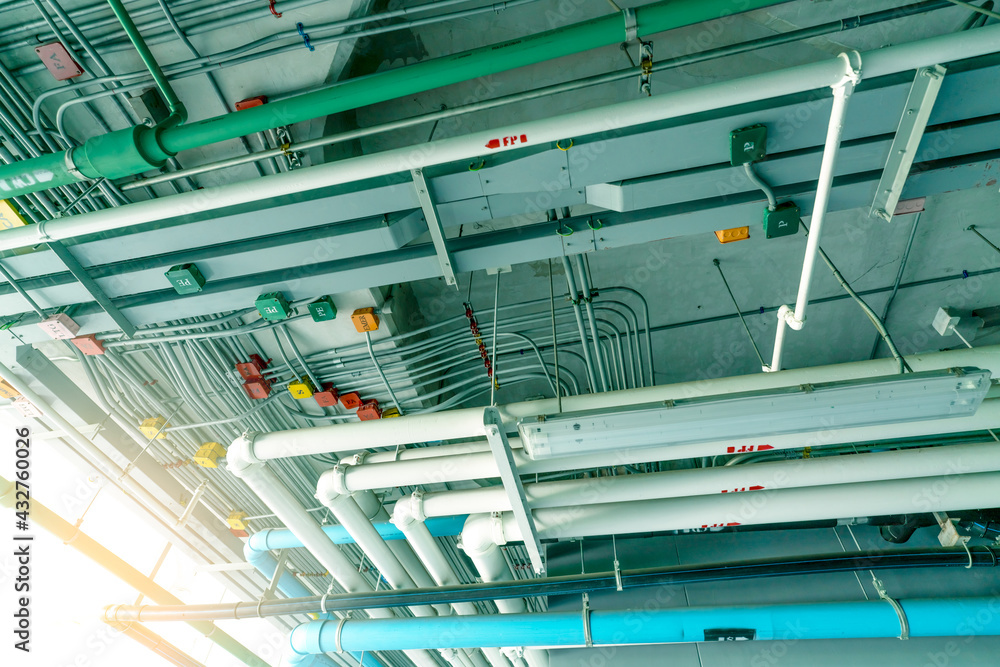 Electrical conduit system and galvanized steel pipe of electric cable  installed on ceiling. PVC plastic pipe of drainage system and clean water  on industrial building ceiling. Building construction. Photos | Adobe Stock