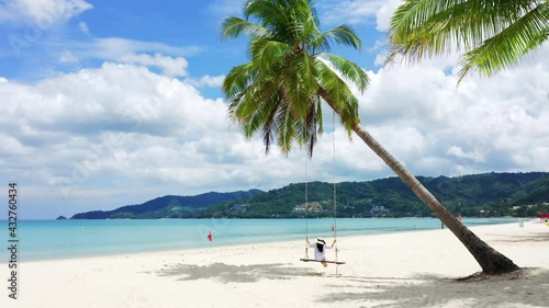 HD Phuket, Thailand. Tropical beach paradise with beach swing with girl in white shirt. Women relax on swing under coconut palm tree at beautiful tropical beach White sand. photo