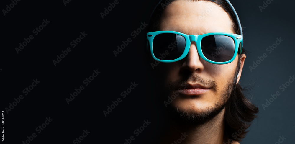 Close-up portrait of young guy wearing cyan sunglasses on black background with copy space.