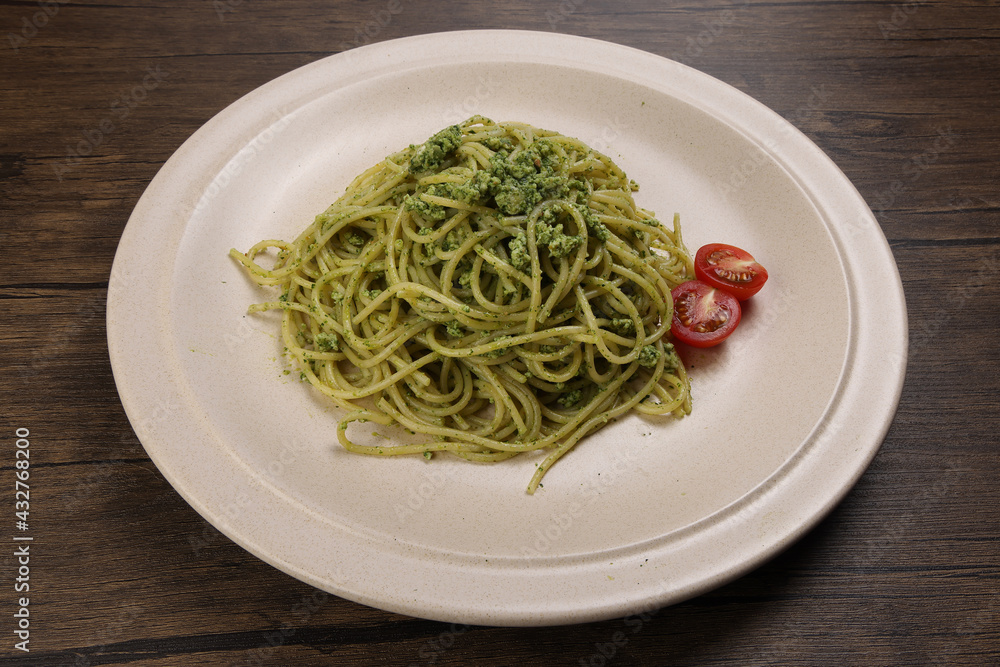 Asian style spaghetti with minced chicken spinach thai basil tomato garlic nutmeg olive oil presto sauce served on badge ceramic plate over on rustic wood background