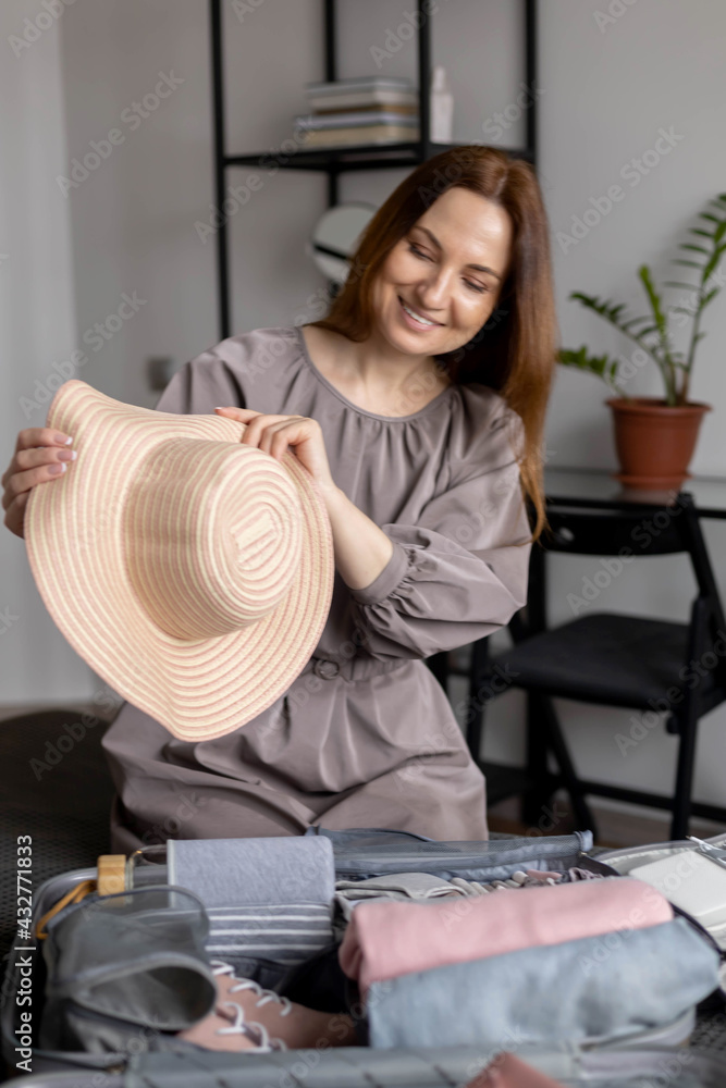Laughing woman posing with straw hat packing baggage getting ready to travel vacation konmari method Laughing woman posing with straw hat packing baggage getting ready to travel vacation konmari method
