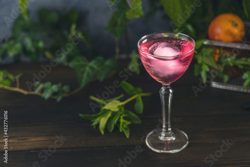 Elegant stemware glass of blood orange cocktail with big ice ball on dark wooden table surface