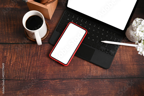 Designer workplace with computer tablet, mobile phone, coffee cup and pencil holder on wooden table.