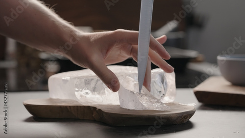 man breaking ice block with knife on olive wood board