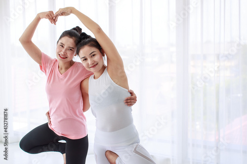 Portrait of a professional female trainer and a lovely student happy practicing yoga in a heart shape pose, smiling and looking at camera. Healthy lifestyle and fitness concept.