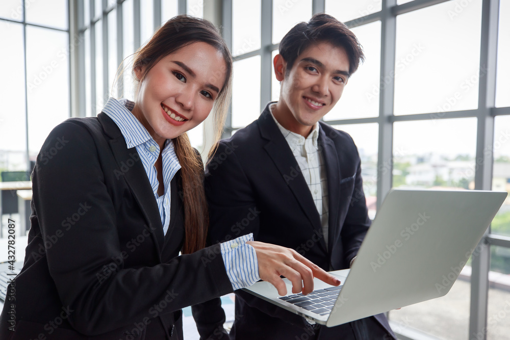 Happy young businessman holding a laptop and pointing at the computer screen talking with his lovely female colleague in the workplace, exciting on a business achievement. Happy young businessman holding a laptop and pointing at the computer screen talking with his lovely female colleague in the workplace, exciting on a business achievement.