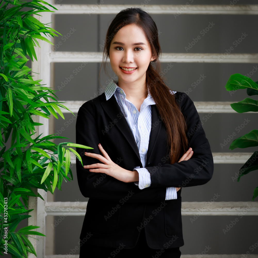 Half length portrait of a beautiful young business woman wearing a stylish black suit with lovely smile, standing in the office, looking at camera. Half length portrait of a beautiful young business woman wearing a stylish black suit with lovely smile, standing in the office, looking at camera.