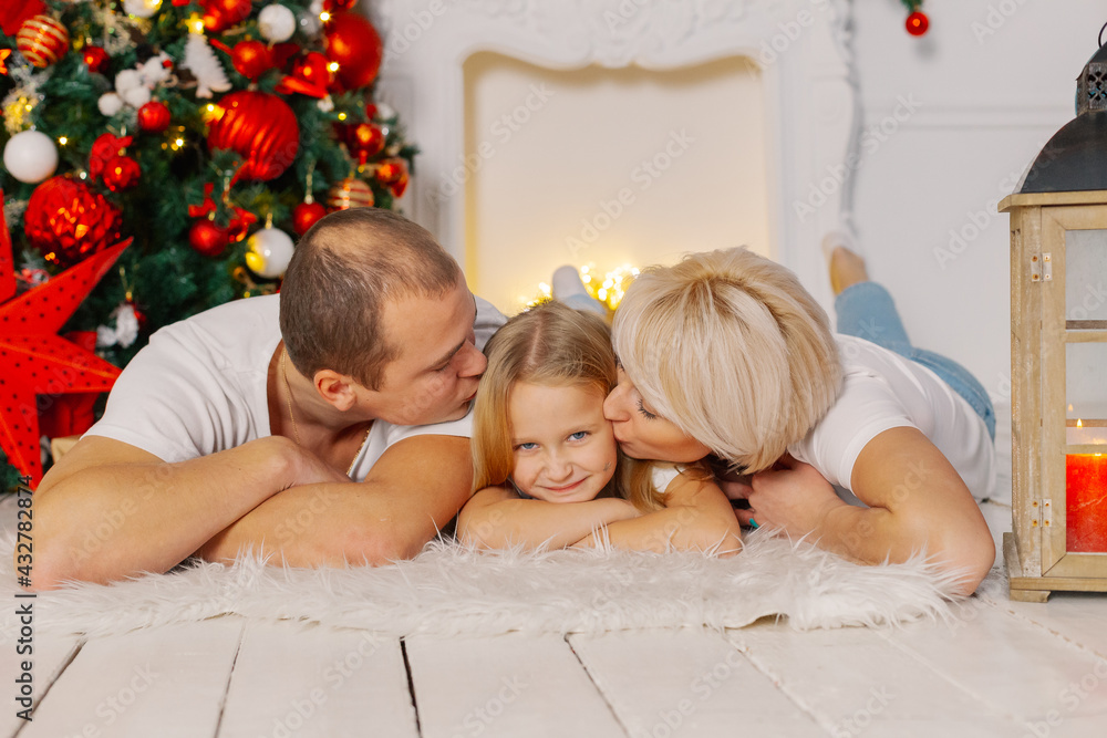 Beautiful young happy family lies on the floor by the Christmas tree. Beautiful young happy family lies on the floor by the Christmas tree.