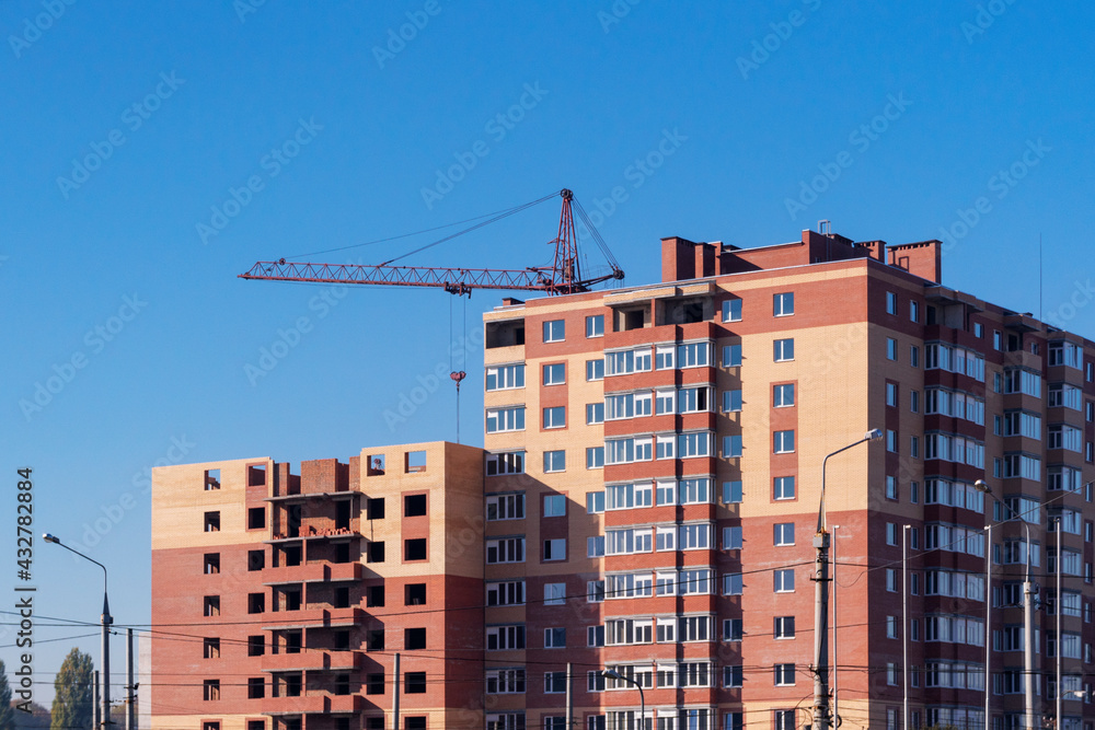 The construction crane and the building against the blue sky. Construction of a high-rise building with a crane. New modern exterior apartment building complex . Concept Construction of housing