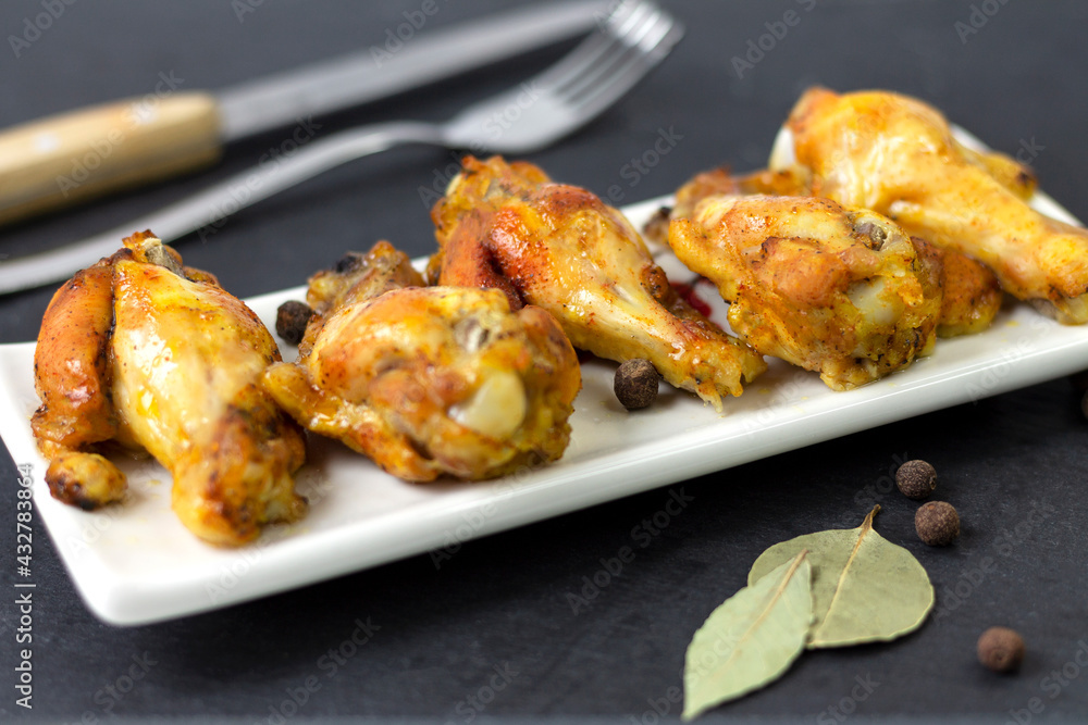 Chicken wings with spices, cooked at home in the oven with yellow tomatoes and green peas, on a dark background. The concept of home cooking and healthy eating.