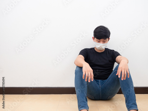 Asian man wearing mask feel drepressed emotion looking down sit on the floor white wall