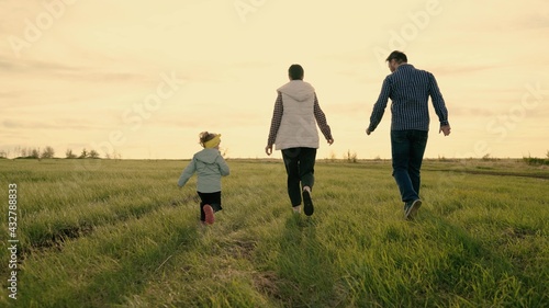 Happy family plays and runs in park at sunset. Family Teamwork. Parents and daughter are running on green grass. Happy family weekend in spring. Children, parents are running. Happy healthy childhood