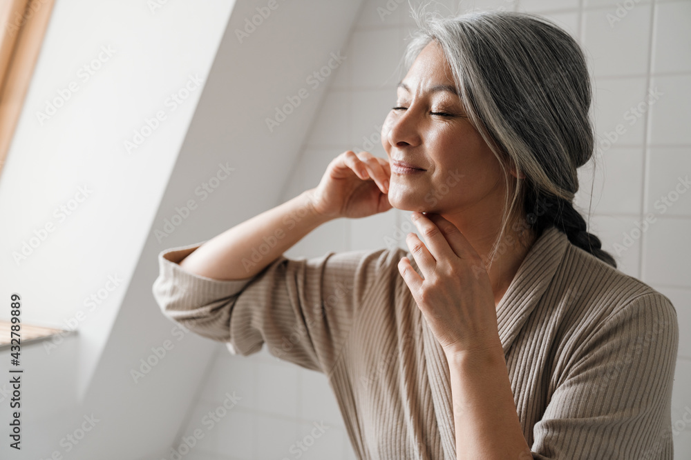 Mature grey woman smiling while getting facial massage in bathroom Mature grey woman smiling while getting facial massage in bathroom