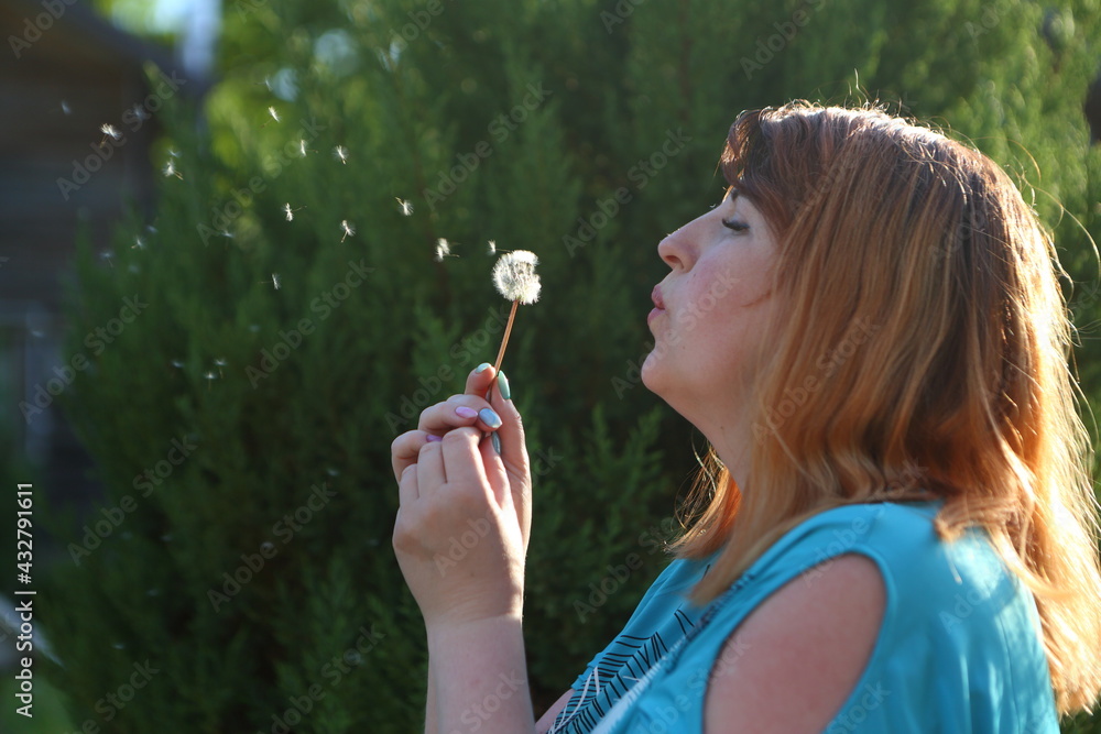 Woman blowing on a dandelion in the park Woman blowing on a dandelion in the park