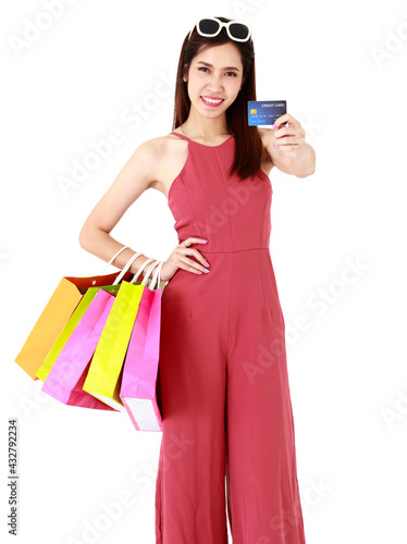 Asian beautiful smiley woman wearing fashion red clothes, sunglasses, holding colorful paper bags, credit card for shopping, payment on isolated white background cutout. Sales Discount Concept.