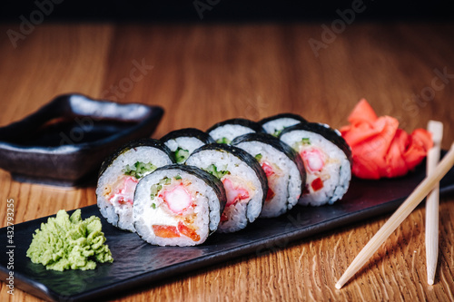 Sushi on a wooden table in restaurant. Portion of sushi served on black plate with wasabi, soy sauce, ginger and chopsticks. Delicious Japanese food. Sliced tasty sushi rolls, close-up