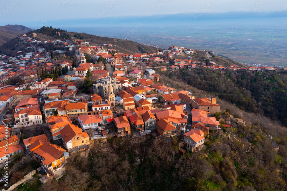 Picturesque aerial view of small Georgian town of Sighnaghi with similar terracotta roofs of houses on steep hill overlooking Alazani Valley in haze on horizon on spring day, Kakheti, Georgia