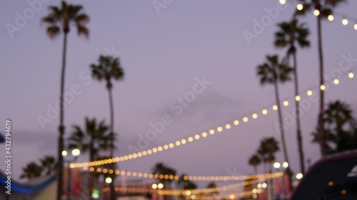 Defocused illuminated electric garland, palm trees silhouettes, Oceanside California USA. Ocean beach tropical pink sunset, pacific coast purple twilight sky. Los Angeles vibes. Bulb lights glowing. © Dogora Sun