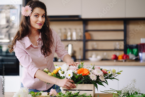 Florist at work: pretty young brunette woman making fashion modern composition of different flowers at home