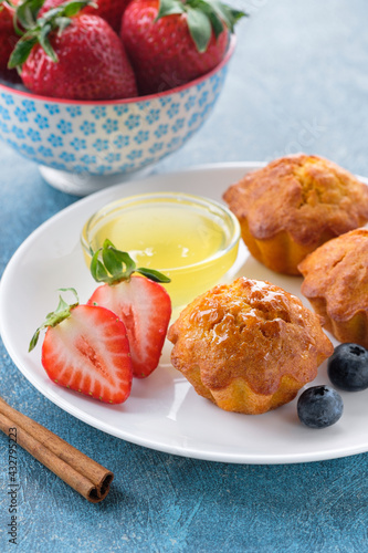 Healthy breakfast - vegan carrot muffins with honey, cinnamon, strawberry and blueberry on white plate. Blue stone background. Copy space.