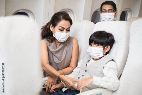 Asian mother helping son to fasten seat belt on airplane seat. People wearing protective mask travel during Coronavirus. safety and security concept for business airline concept