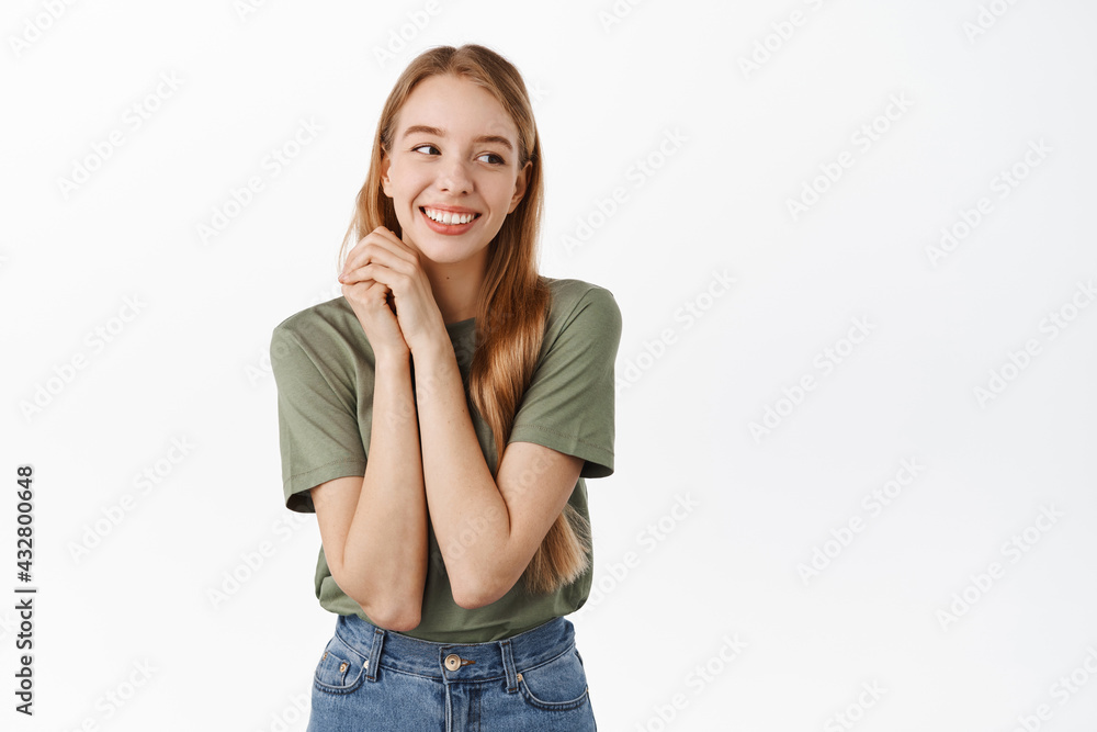 Romantic tender blond girl, holding hands near face and daydreaming, gazing at something lovely and cute, standing in t-shirt against white background Romantic tender blond girl, holding hands near face and daydreaming, gazing at something lovely and cute, standing in t-shirt against white background