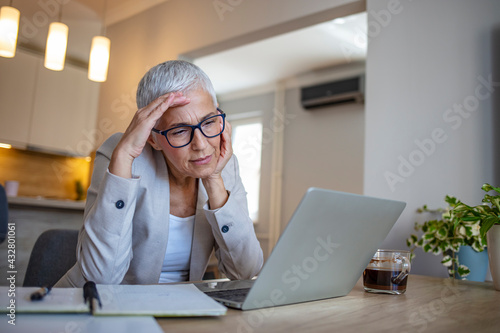 Upset, unhappy, pretty, charming, professional teacher feeling bad, took off glasses, touching her temple, suffering from headache, sitting at desk in workstation, having computer, tablet on the table photo