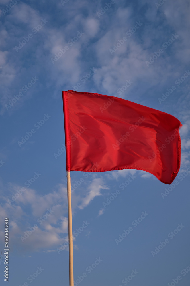 Red flag with blue sky with clouds, strong wind flying red flag. Red