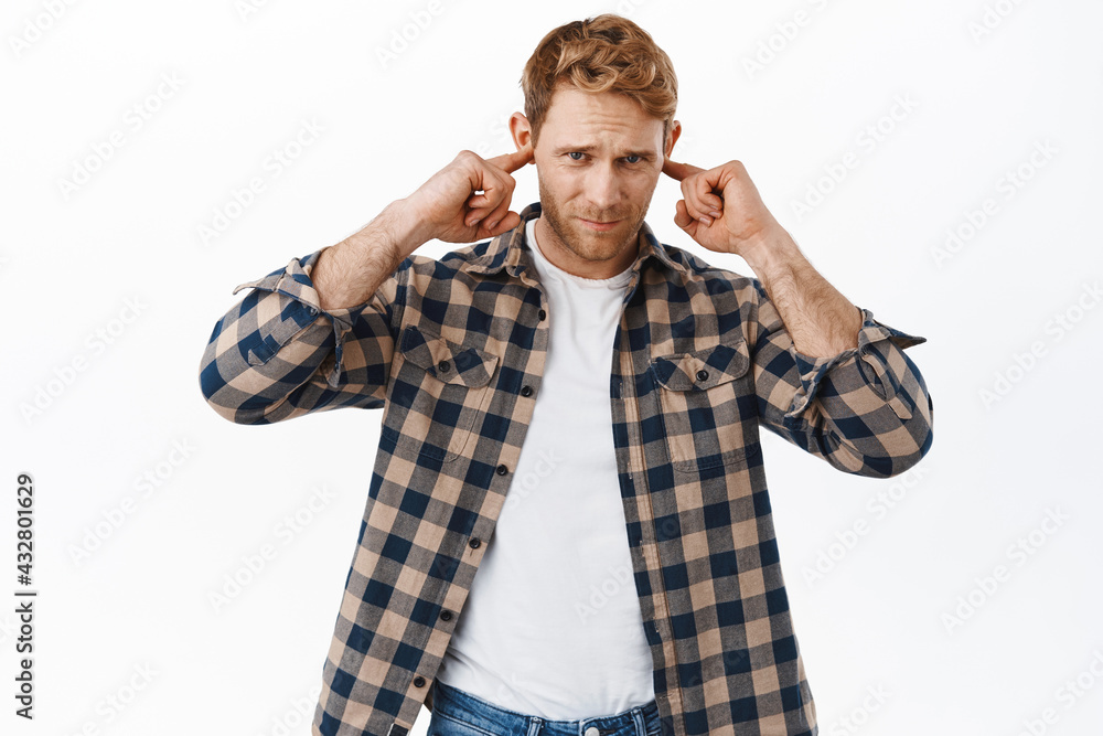 Distressed redhead adult man cover his ears, plug fingers in earholes and looking bothered by annoying loud noise, unwilling to hear something, standing over white background Distressed redhead adult man cover his ears, plug fingers in earholes and looking bothered by annoying loud noise, unwilling to hear something, standing over white background