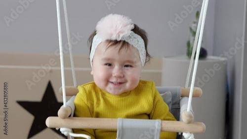 Cute one year baby sitting in door frame swing and changing face expressions from neutral to overexcited and joyful, clapping hands and move from side to side smiling photo