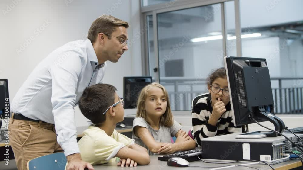 Computer science teacher discussing task with schoolchildren. Excited multiethnic children sitting in front of monitor, doing assignment with help of tutor. Education, informatics concept. Computer science teacher discussing task with schoolchildren. Excited multiethnic children sitting in front of monitor, doing assignment with help of tutor. Education, informatics concept.
