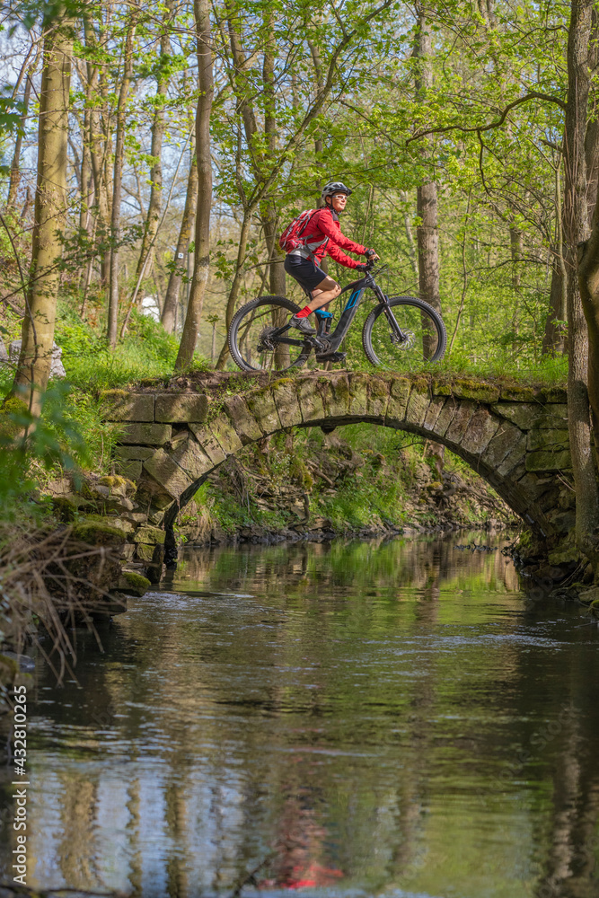 Naklejka premium nice active senior woman riding her electric mountain bike in early spring along the little river Glems near Stuttgart, Baden-Wuerttemberg, Germany 