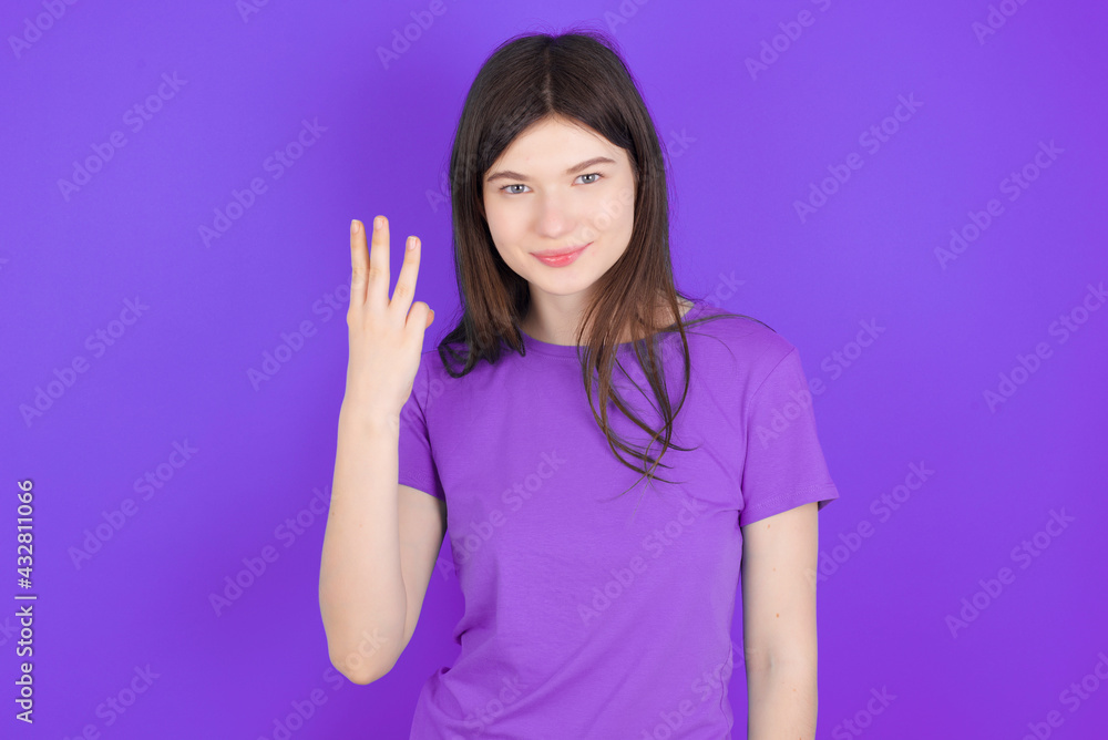 young beautiful Caucasian girl wearing purple T-shirt over purple background smiling and looking friendly, showing number three or third with hand forward, counting down young beautiful Caucasian girl wearing purple T-shirt over purple background smiling and looking friendly, showing number three or third with hand forward, counting down