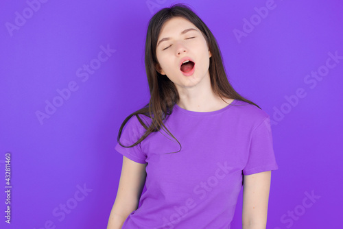 young beautiful Caucasian girl wearing purple T-shirt over purple background yawns with opened mouth stands. Daily morning routine