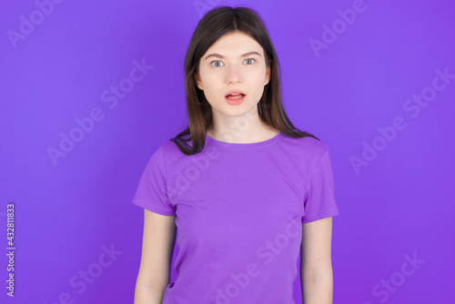 Shocked young beautiful Caucasian girl wearing purple T-shirt over purple background stares bugged eyes keeps mouth opened has surprised expression. Omg concept © Jihan