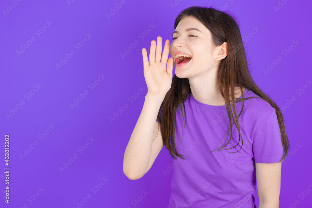 young beautiful Caucasian girl wearing purple T-shirt over purple background look empty space holding hand near her face and screaming or calling someone. young beautiful Caucasian girl wearing purple T-shirt over purple background look empty space holding hand near her face and screaming or calling someone.