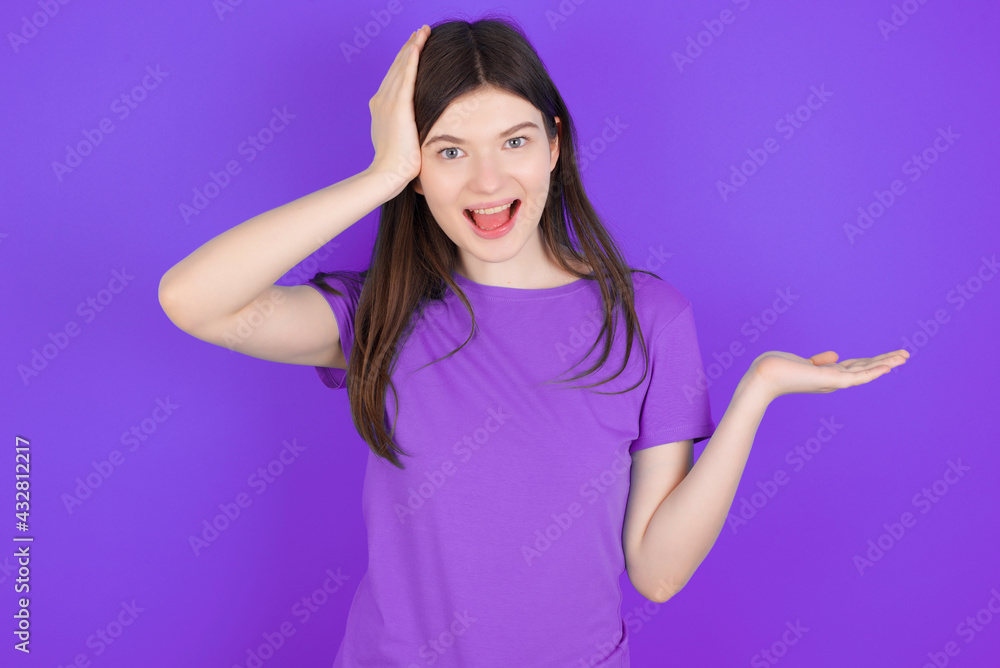 Shocked amazed surprised young beautiful Caucasian girl wearing purple T-shirt over purple background hold hand offering proposition Shocked amazed surprised young beautiful Caucasian girl wearing purple T-shirt over purple background hold hand offering proposition