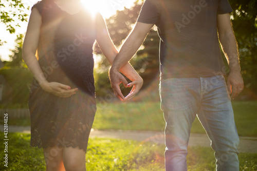 Eine junge schwangere Frau und ein Mann formen mit Ihren Händen ein Herz. Gegenlichtaufnahme photo