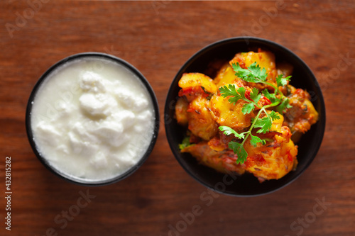 Close-up of Indian vegetarian dish of spicy Potato and Tomato curry garnished with green coriander fresh leaves with curd. over wooden background.
